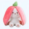 Une peluche de lapin blanc cachée sous une fraise rose. La fraise a une feuille verte sur le dessus.