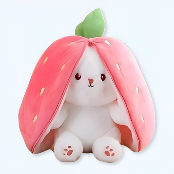 Une peluche de lapin blanc cachée sous une fraise rose. La fraise a une feuille verte sur le dessus.