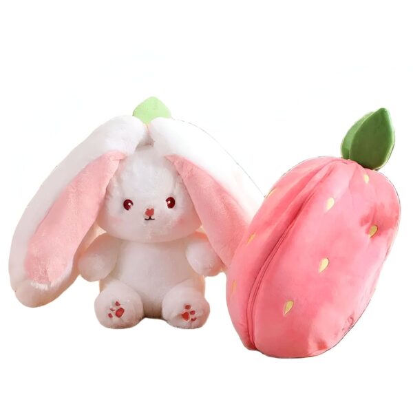 Un lapin en peluche blanc avec de grandes oreilles roses et une fraise en peluche rose.
