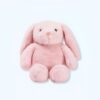 Une peluche rose en forme de lapin assis sur un fond blanc.