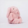 Une peluche rose en forme de lapin assis sur un fond blanc.