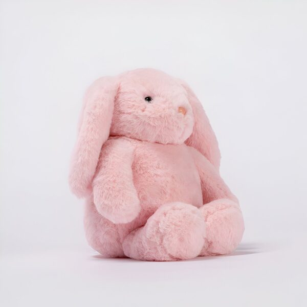 Une peluche rose en forme de lapin assis sur un fond blanc.