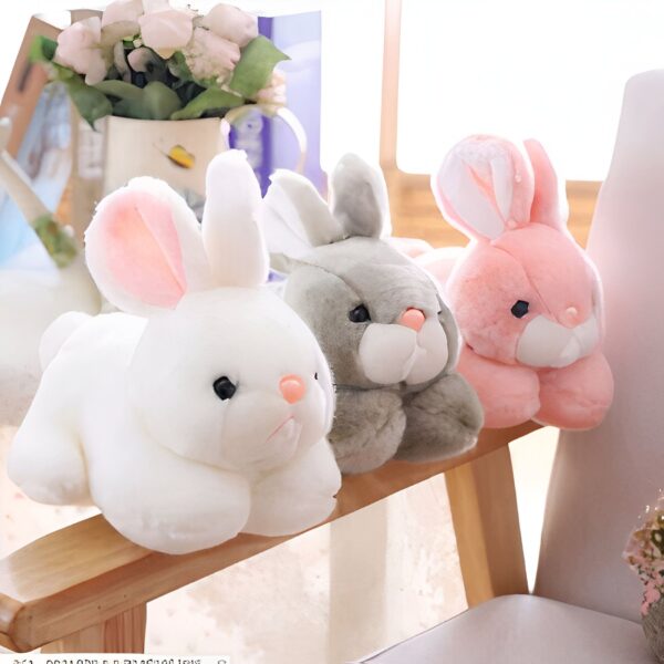 peluche-lapin-rose-tout-doux-2a Trois lapins en peluche, un blanc, un gris et un rose, sont assis sur un banc en bois.