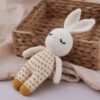 Un lapin en crochet blanc avec un pyjama jaune et blanc repose dans un panier en osier.
