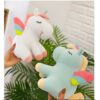 Deux peluches de licorne, l'une blanche avec des ailes roses, l'autre bleue avec des ailes colorées, sont présentées dans une main.