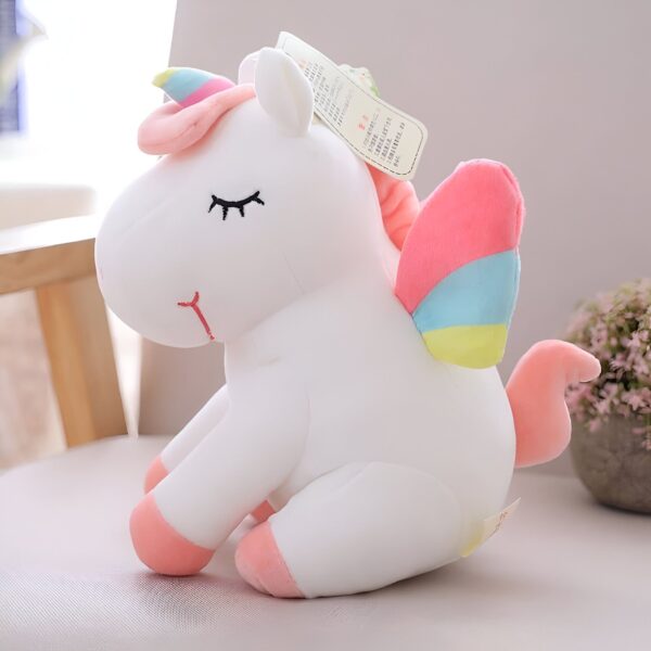 Peluche licorne blanche avec des ailes arc-en-ciel et des détails roses.
