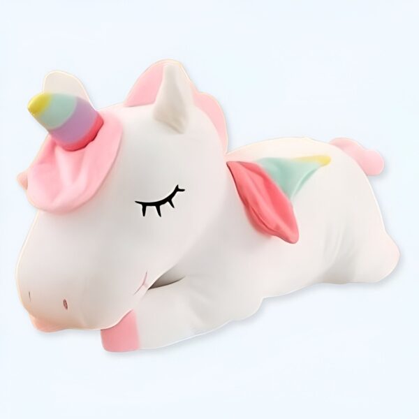 Une peluche blanche en forme de licorne avec une corne arc-en-ciel et des ailes roses, couchée sur le côté, les yeux fermés.