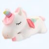 Une peluche blanche en forme de licorne avec une corne arc-en-ciel et des ailes roses, couchée sur le côté, les yeux fermés.