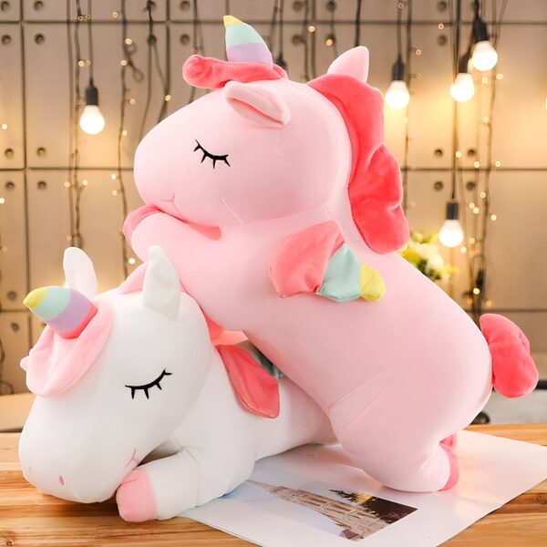 Deux licornes en peluche, l'une rose et l'autre blanche, se blottissent l'une contre l'autre sur un fond de lumières scintillantes.