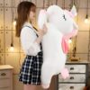 Une jeune femme tenant une grande peluche en forme de licorne blanche avec des détails roses.