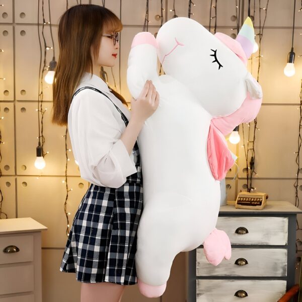 Une jeune femme tenant une grande peluche en forme de licorne blanche avec des détails roses.