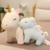 peluche-licorne-bleu-ailes-dorees-jouet-enfant-2a Deux licornes en peluche, une blanche et une bleue, sont assises côte à côte. La licorne blanche a une corne dorée et des sabots roses, tandis que la licorne bleue a des ailes blanches et des sabots bleus. Les deux licornes ont les yeux fermés et sourient.