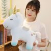 peluche-licorne-bleu-ailes-dorees-jouet-enfant-3a Une jeune femme tient une peluche licorne bleue avec des ailes et une corne dorée. La licorne a deux étoiles jaunes et roses sur son flanc.