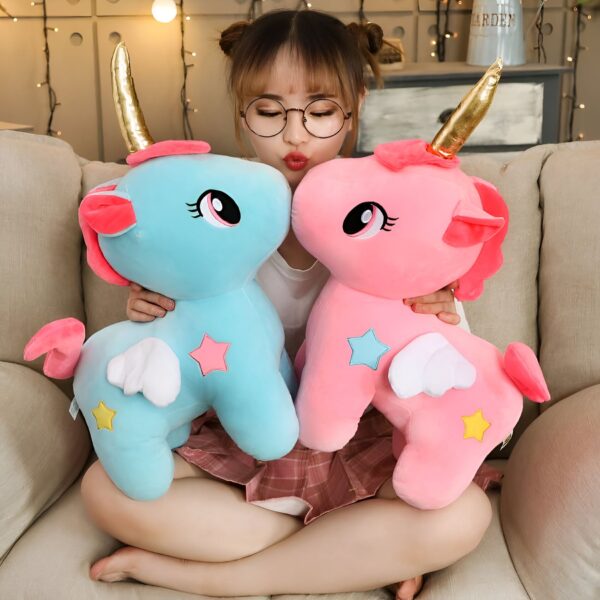 Une jeune femme assise sur un canapé, tenant deux peluches en forme de licorne, l'une bleue et l'autre rose, avec des ailes et des étoiles.