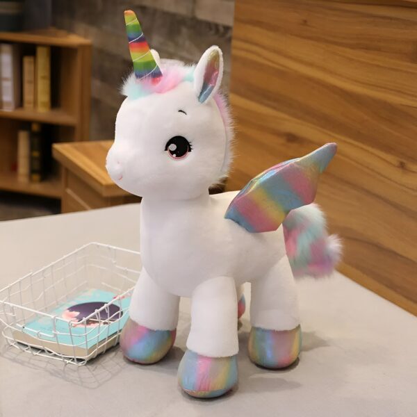 Une peluche de licorne blanche avec une corne arc-en-ciel, des ailes arc-en-ciel et des pieds arc-en-ciel.