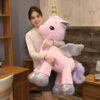 Une jeune femme tient une grande peluche rose en forme de licorne avec une corne arc-en-ciel. La licorne a des ailes arc-en-ciel et une queue de fourrure arc-en-ciel.