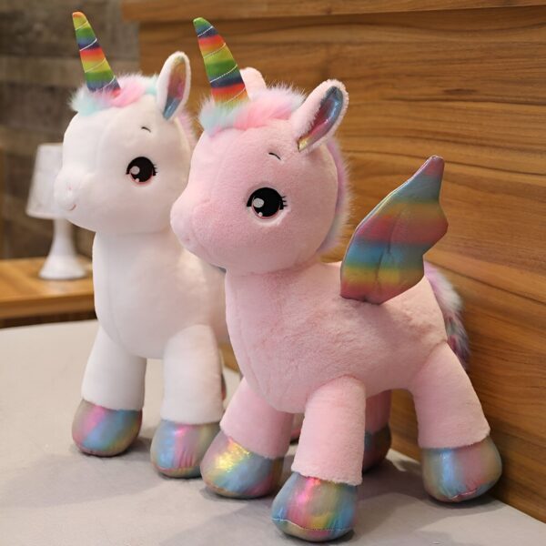Deux peluches licorne, une blanche et une rose, avec des ailes arc-en-ciel. Les licornes ont de grands yeux noirs et des cornes multicolores.