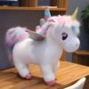 Une peluche de licorne blanche avec une crinière et une queue arc-en-ciel. La licorne a des ailes arc-en-ciel et des yeux noirs.