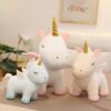 Trois peluches de licorne, une grande blanche, une moyenne rose et une petite bleue, avec des ailes et des cornes dorées.
