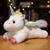 Une peluche blanche en forme de licorne avec des ailes argentées et une crinière arc-en-ciel. La licorne est couchée sur un fond en bois.