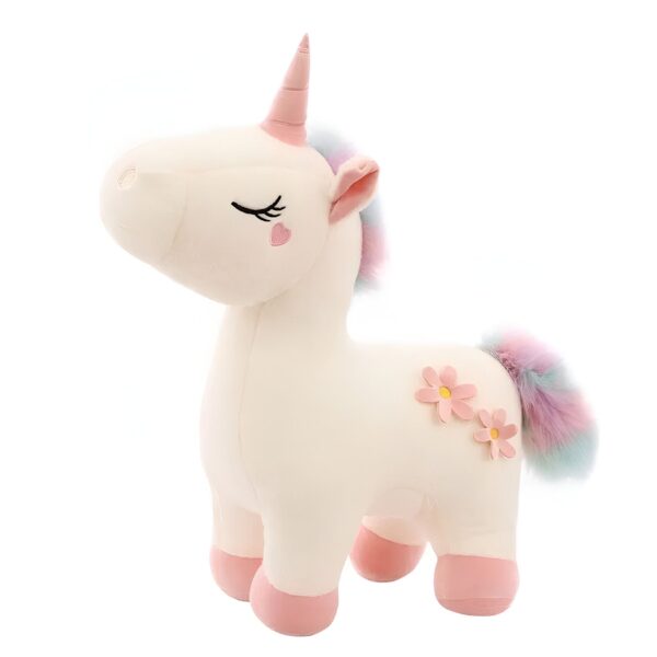 Une peluche de licorne blanche avec une crinière arc-en-ciel, des fleurs roses et un petit cœur sur la joue.