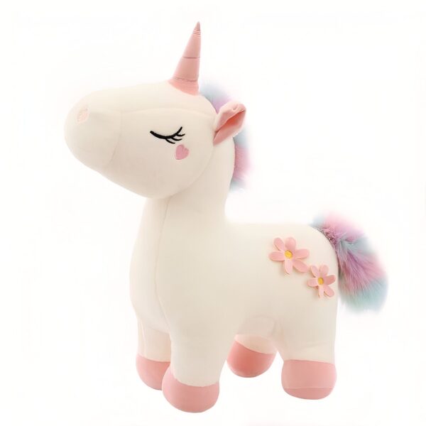 peluche-licorne-magique-douce-cadeau-enfant-6a-1 Une peluche de licorne blanche avec une crinière arc-en-ciel, des fleurs roses et un petit cœur sur le visage.