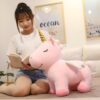 Une jeune femme assise sur un lit, tenant une grosse peluche de licorne rose avec une corne dorée. La licorne a des étoiles sur ses ailes.