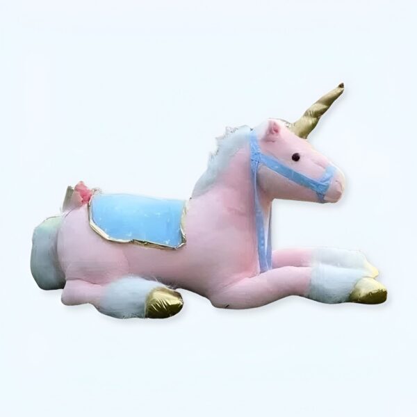 Une licorne rose en peluche avec une selle bleue et une corne dorée, allongée sur le ventre.