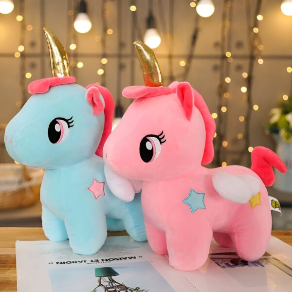 Deux peluches en forme de licorne, l'une bleue et l'autre rose, avec des ailes blanches et une étoile sur le flanc. Elles ont des yeux noirs et des cornes dorées.