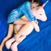 Une jeune femme endormie enlaçant une peluche licorne rose sur un drap bleu.