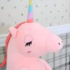 Gros plan sur la tête d'une peluche rose en forme de licorne avec une corne arc-en-ciel. La licorne a les yeux fermés et un air rêveur.