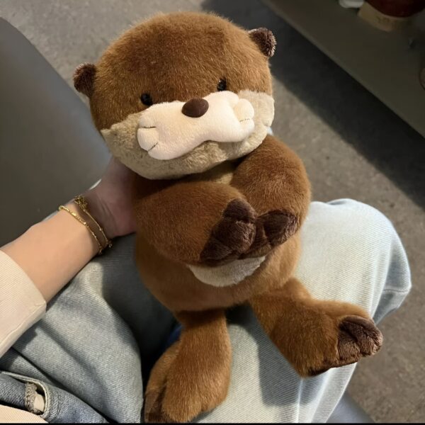 Une peluche de loutre marron tenant ses pattes devant elle, assise sur les genoux d'une personne.