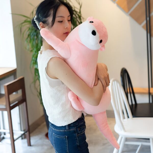 peluche-loutre-rose-jouet-doux-pour-bebe-et-enfant-cadeau-original-5a Une jeune femme en jean bleu serré tenant une grande peluche rose en forme de loutre.