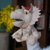 Marionnette de dinosaure Tricératops en peluche grise avec de grands yeux jaunes, portée par une main.