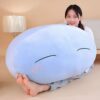 Une jeune femme souriante tenant une grande peluche bleue en forme de blob avec un visage mignon.