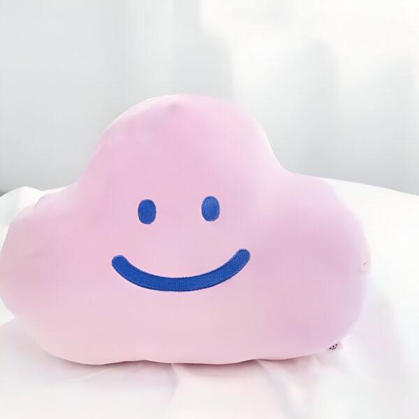 Un oreiller en forme de nuage rose avec un sourire bleu brodé.