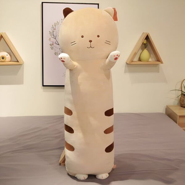 Un long coussin en forme de chat beige avec des détails marrons et des pattes roses, placé sur un lit.