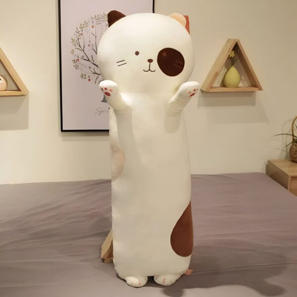 Un long coussin en forme de chat blanc avec des détails marrons, debout sur un lit.