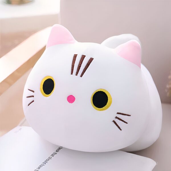 Une peluche blanche en forme de chat avec des yeux jaunes, un nez rose et des moustaches brunes.