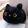 Un coussin noir en forme de chat avec des yeux jaunes et un petit nez rose.