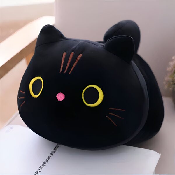 Un coussin noir en forme de chat avec des yeux jaunes et un petit nez rose.