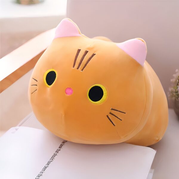 Coussin en forme de chat orange avec de grandes oreilles roses et des yeux noirs et jaunes.