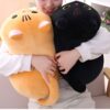 Une femme tient deux peluches en forme de chat, un chat noir et un chat orange.