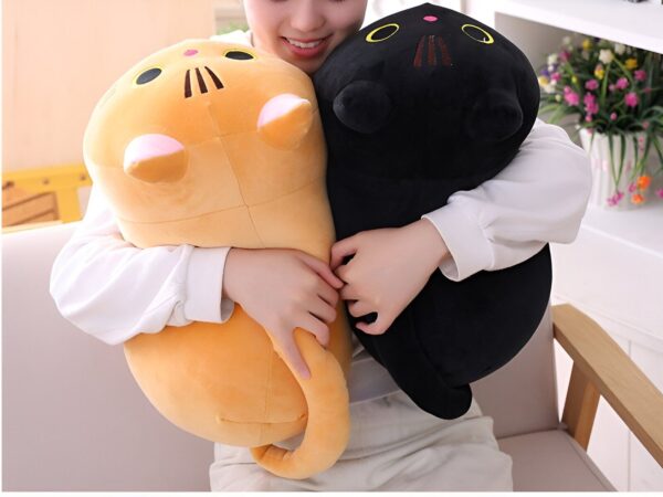 Une femme tient deux peluches en forme de chat, un chat noir et un chat orange.