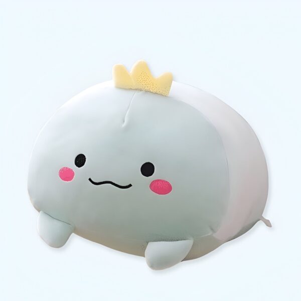 Une peluche bleu clair en forme de baleine avec une couronne jaune sur la tête et un visage souriant avec des joues roses.