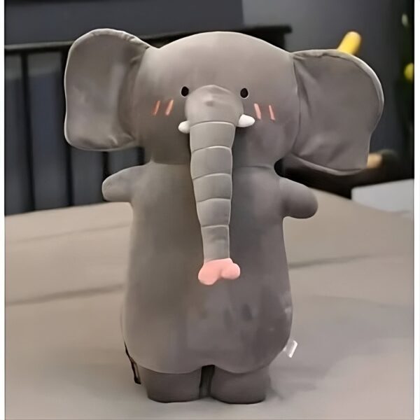 peluche-oreiller-elephant-3a Une peluche d'éléphant en gris avec des détails roses sur son visage et ses pieds. L'éléphant est debout sur une surface claire.