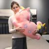 Une jeune femme tenant un grand coussin en forme de licorne rose avec des étoiles.