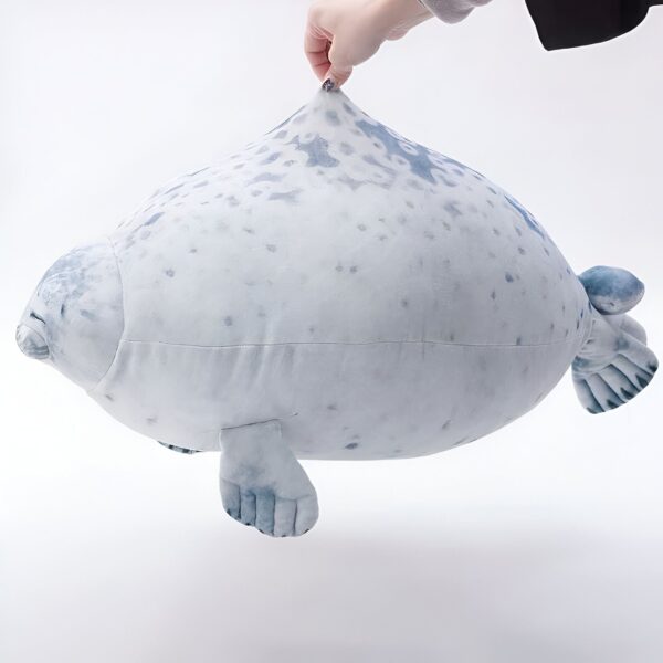 peluche-oreiller-phoque-doux-et-adorable-pour-enfant-3a-1 Une peluche de phoque gris et blanc avec des points noirs, flottant dans les airs, avec une main tenant le haut de la peluche.
