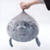 peluche-oreiller-phoque-doux-et-adorable-pour-enfant-4a-1 Une peluche de phoque gris en forme de boule, flottant dans l'air avec une main qui la soulève par le haut.
