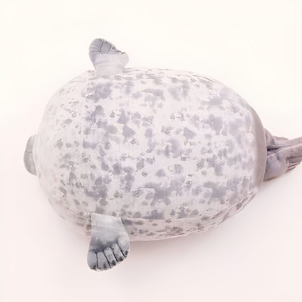 peluche-oreiller-phoque-doux-et-adorable-pour-enfant-6a-2 Un phoque gris allongé sur le dos, vu de dessus.